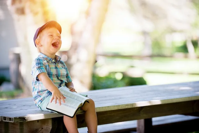 Laughing Kid Reading a Book on a Bench